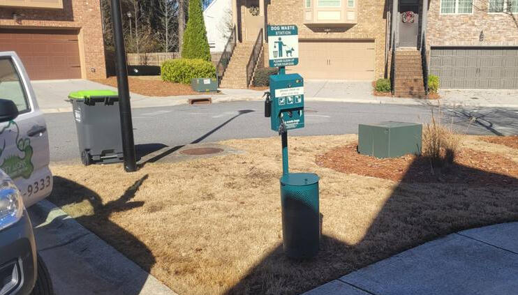 A teal Dirty Work pet waste station on a townhome community street, photographed on a service visit